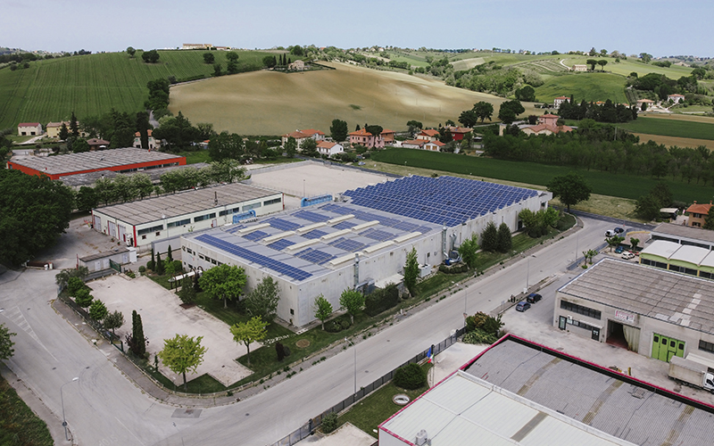 Stabilimento industriale, pannelli solari, energia rinnovabile, veduta aerea, paesaggio collinare.