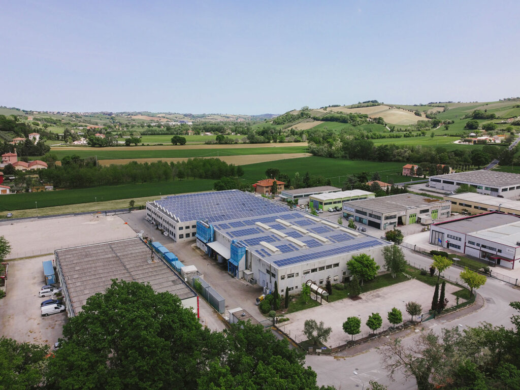 Stabilimento industriale, pannelli solari, energia rinnovabile, veduta aerea, paesaggio collinare.