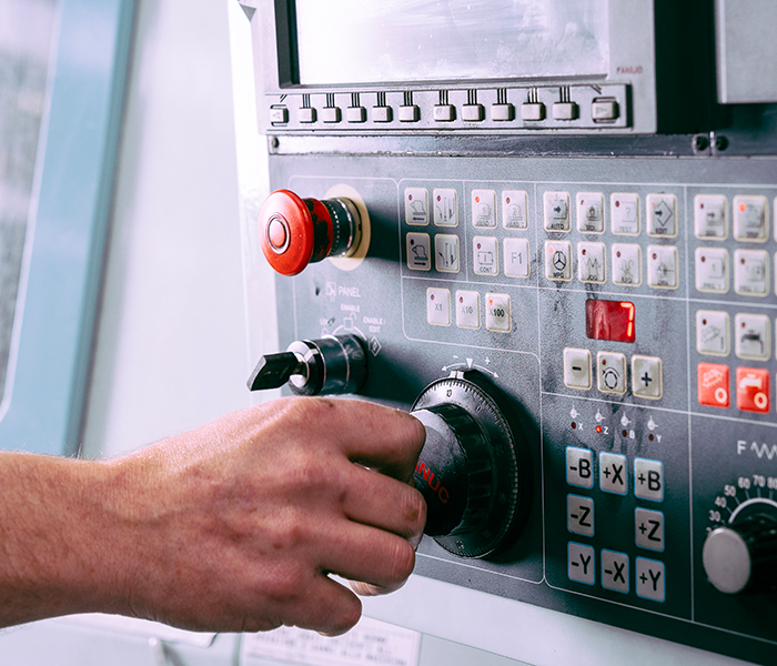 mano su pannello CNC, regolazione macchina utensile, controllo manuale CNC.